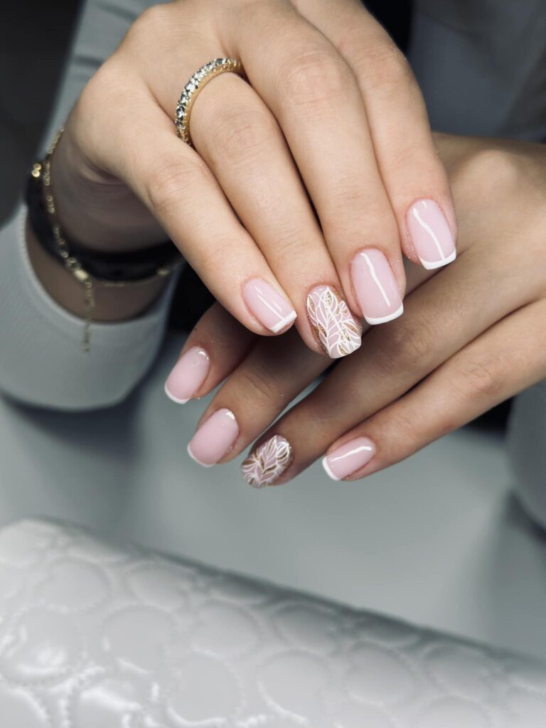 Delikatny manicure w odcieniu pudrowego różu z białymi zdobieniami i subtelnym french manicure.