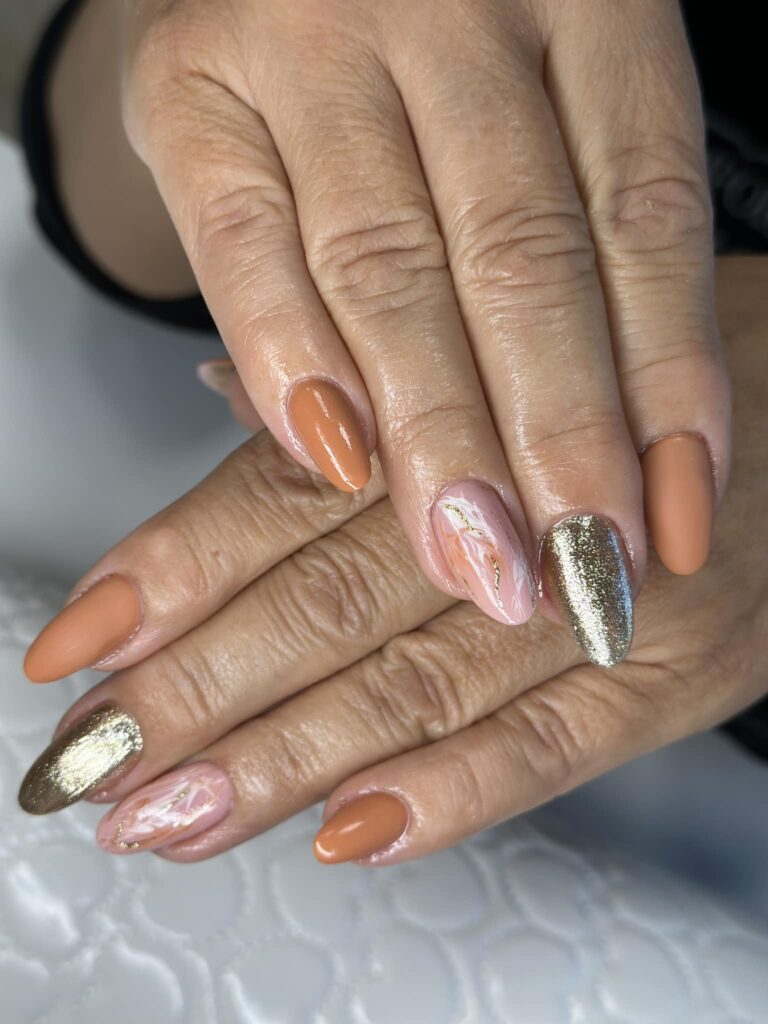 Jesienny manicure w odcieniach brzoskwini, różu i złota z delikatnym marmurkowym zdobieniem.