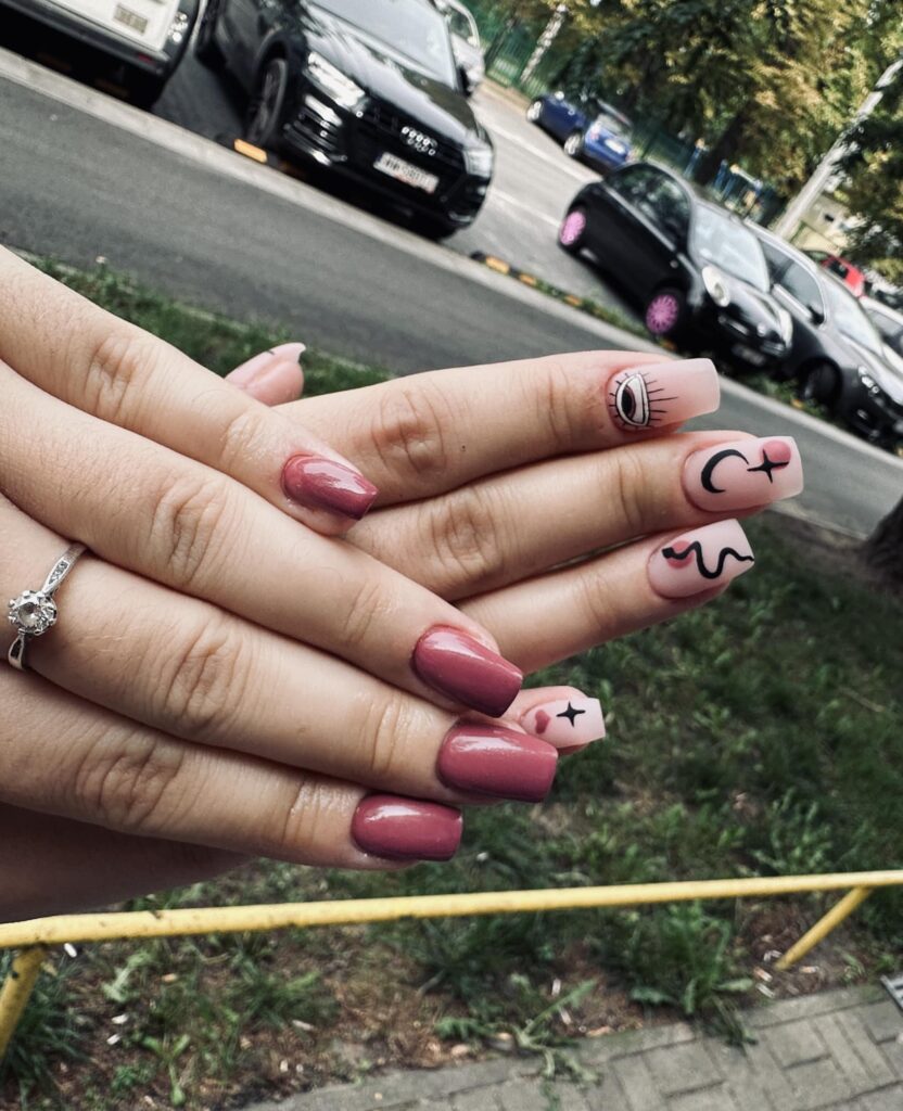 Różowy manicure z czarnymi minimalistycznymi zdobieniami i motywem oka.
