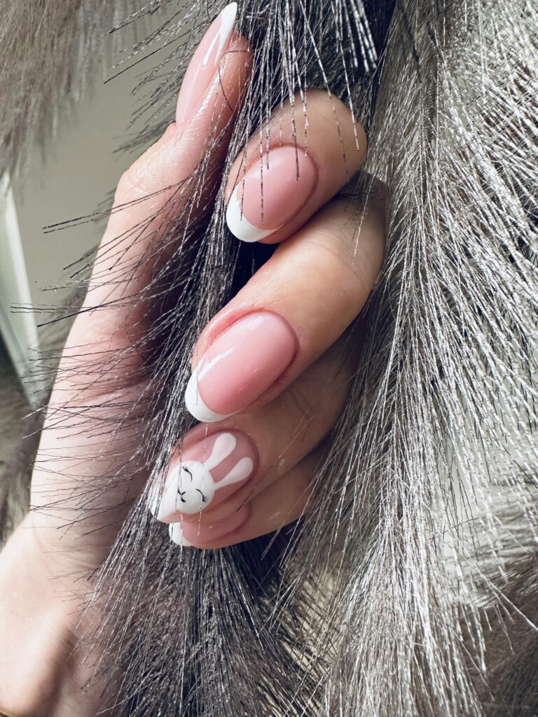 Delikatny różowy manicure z białym french i króliczkiem na paznokciu.